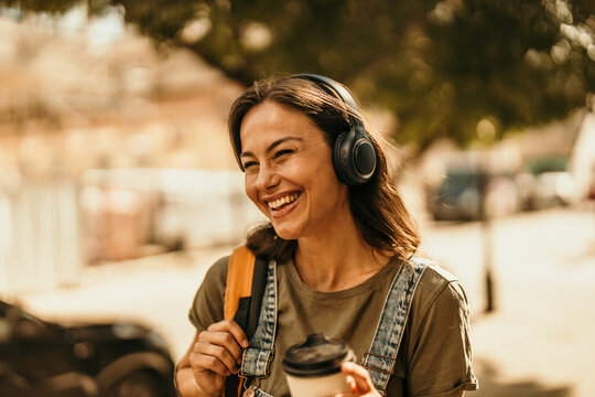 Happy woman listening to music outdoors with coffee