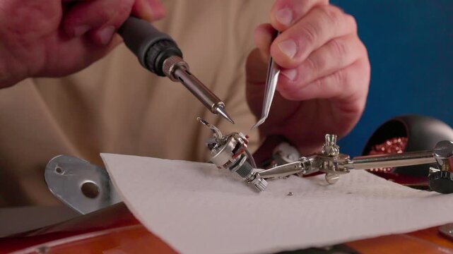 Close-up view of hands soldering metal electronics components as molten solder bead forms fresh electrical joint under warm focused light
