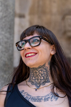 Happy young woman with neck and chest tattoos and piercings smiling and looking up outside