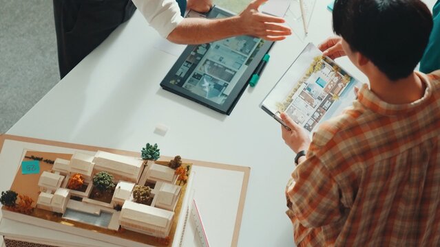 Professional architect engineer sitting while explain house plan to manager. Aerial view of smart designer looking blueprint while talking about building construction at meeting room. Alimentation.