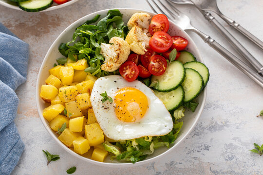 Healthy breakfast or lunch bowl with cooked potatoes, fresh vegetables and fried egg
