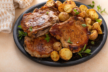 Pork chops on a bone grilled or sauteed served with roasted potatoes on a plate