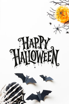 Happy Halloween lettering framed by black and orange roses, spiderwebs, bats and skeleton hands on white, ideal for cards, invitations, posters and seasonal advertising.