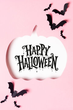 Happy Halloween lettering on a white pumpkin shape with flying black bats on a pink background, ideal for greeting cards, invitations, posters and seasonal advertising.