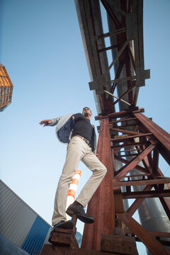 Dynamic businessman balancing on giant industrial steel structure metaphor for corporate freedom with copy space