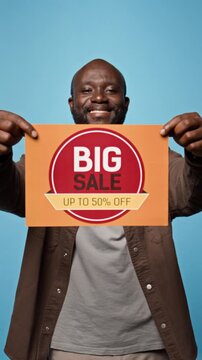 Portrait of smiling African American man showing big sale discount sign. Suitable for retail marketing, e-commerce social media promotions and discount advertising, vertical
