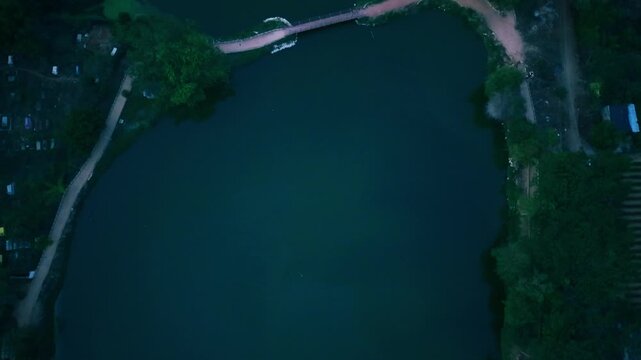 A serene top-down aerial perspective capturing a narrow, meandering river or swamp channel flowing through a vibrant, dense green ecosystem of trees, plants, and natural marshes in Bengaluru.