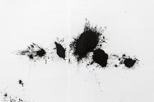Black powdered toner is spilled on white paper on a table after being replaced in a laser printer cartridge.