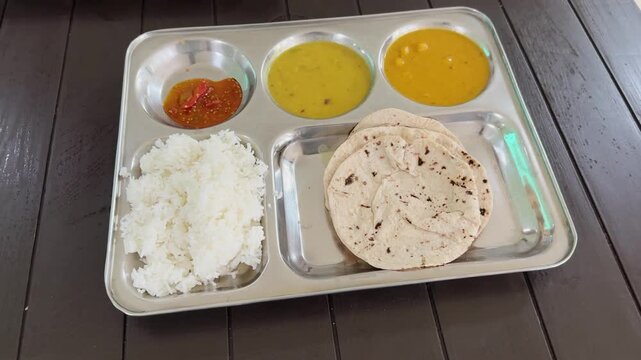 Camera orbiting shot of a traditional Indian thali featuring steamed rice roti dal curry and spicy pickle served in a stainless steel tray