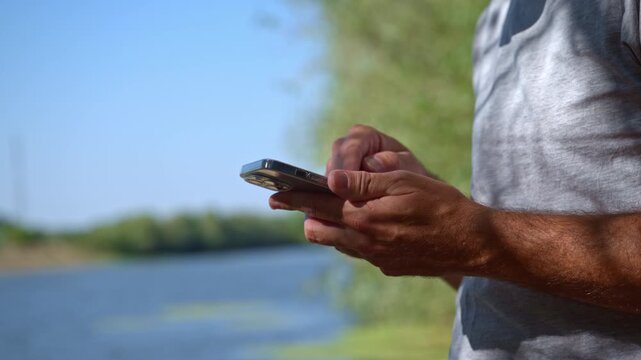 Man attentively checking his mobile phone on a riverbank. Concept of outdoor digital connectivity, location navigation, remote work, thoughtful communication, and modern leisure lifestyle. 4K.