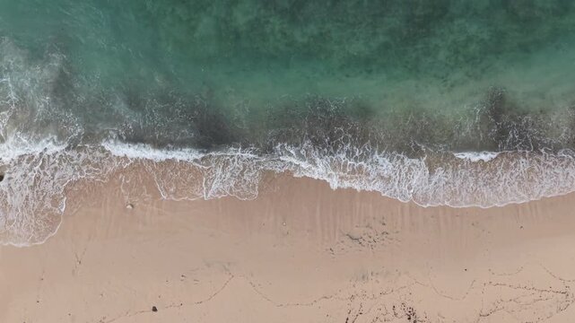 Aerial view of a sandy beach and shoreline with rolling ocean waves, foamy surf and scattered footprints offering a calm, minimal coastal landscape perfect for travel, nature and summer themes