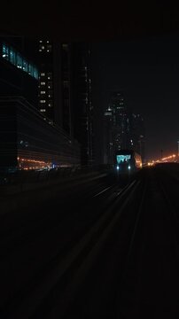 DUBAI, UAE - AUGUST 29, 2026: Dubai Metro train approaches on an elevated railway and passes the camera beside illuminated towers in UAE at night