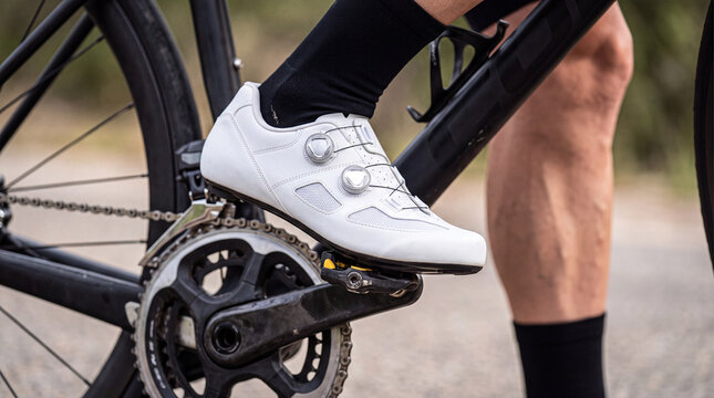 Close-up of cyclist wearing white cycling shoe clipped into road bike pedal for performance training