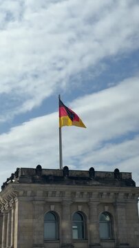 German flag on Bundestag top under blue sky with puffy clouds. Main symbol of Germany on parliament building in Berlin close up