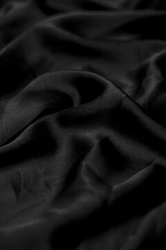 Luxurious black silk fabric with gentle folds and waves presents a smooth texture and elegant drape for fashion and design concepts