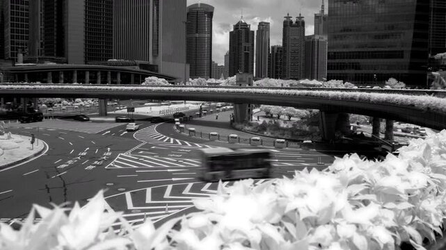 An infrared timelapse shows traffic moving through the Lujiazui road intersection in Pudong, Shanghai, with modern skyscrapers and a pedestrian bridge under a cloudy sky