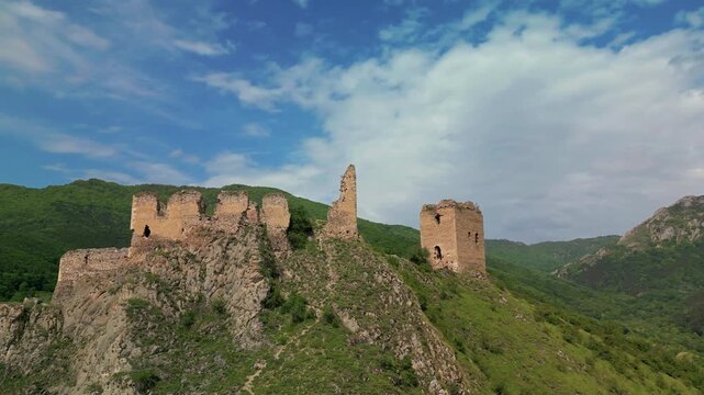 Medieval fortress ruins standing on a rocky mountain slope with green hills and blue sky