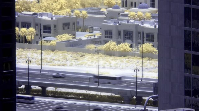 Infrared timelapse shows cars speeding along a highway overpass in a modern city with luxury residential villas and palm trees nearby