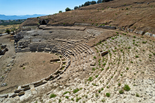 Aerial view of the ancient theater of Sicyon in Corinthia, Greece, showing its semicircular cavea, stepped stone seating, orchestra, stage foundations and surviving architectural remains.