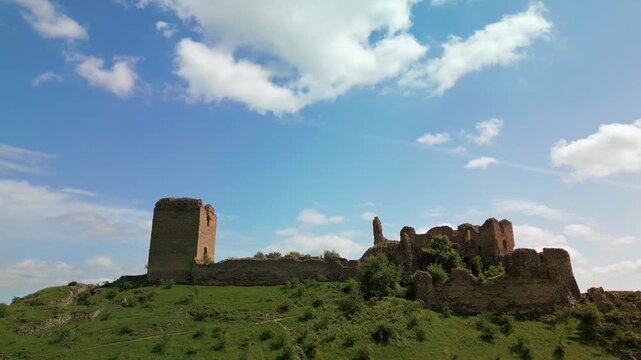 Medieval fortress ruins standing on a rocky mountain slope with green hills and blue sky