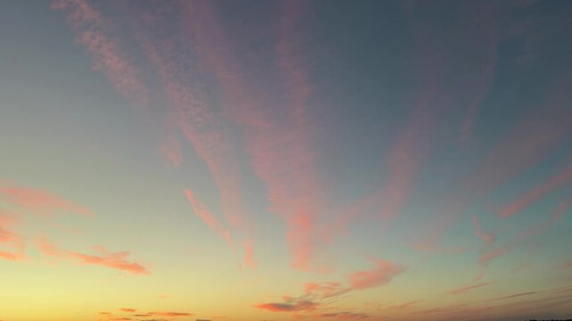 The sunset sky with thin, pink, feathery clouds, illuminated by warm hues, contrasts with the yellow and turquoise sky.