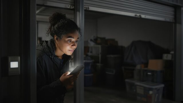Woman Checking Phone Outside Dark Storage Unit at Night