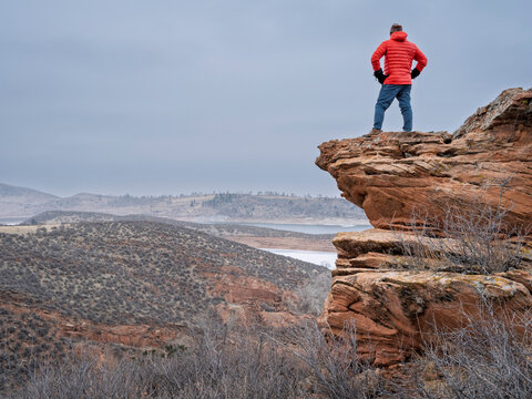male hiker on a rocky cliff  at foothills of Rocky Mountains, Horsetooth Reservoir area - a popular recreational area in northern Colorado in fall or winter scenery with falling snow