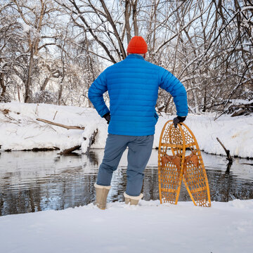 male hiker with classic wooden snowshoes (Bear Paw) on a stream shore, winter scenery in Colorado