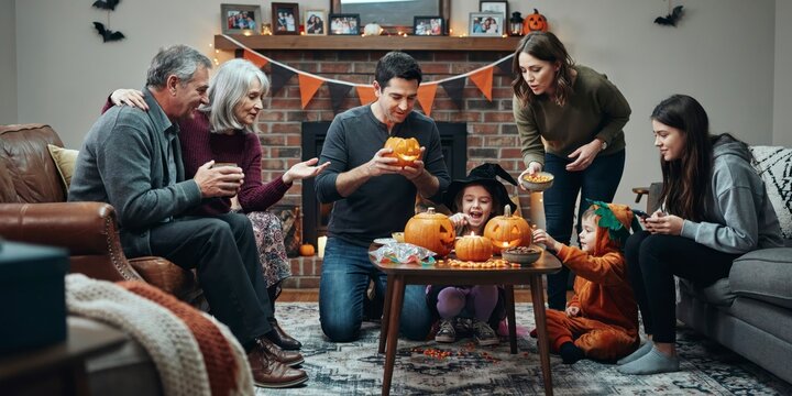 Multigenerational family having fun carving pumpkins together at home for halloween, happy halloween, halloween celebration theme
