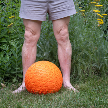 legs of senior man with a heavy slam ball in backyard