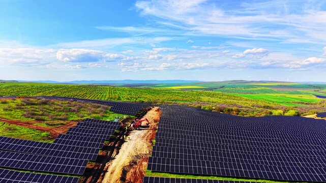 Aerial view of solar panel array reaching distant hills. Drone shot of dense panel rows with worker figures and mountain range visible on the horizon.