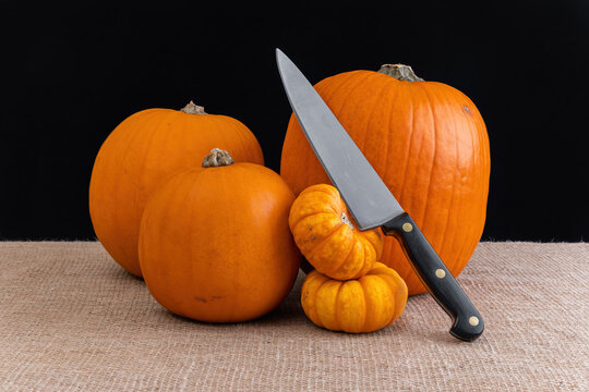 Pumpkins and chef's knife on hessian with black background