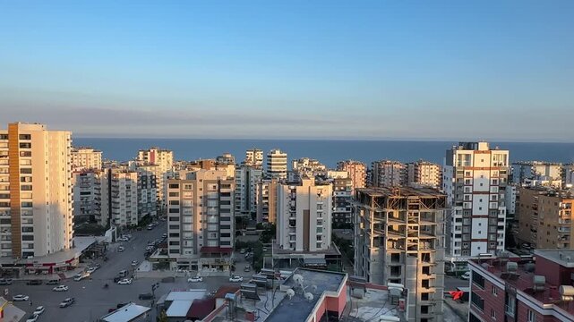 Pan across modern residential buildings in Mezitli, Mersin, with the blue Mediterranean Sea stretching along the horizon.