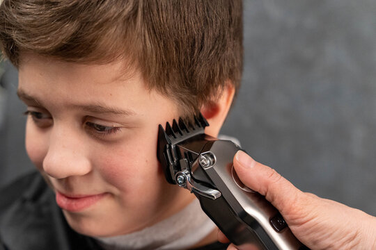 Boy getting a haircut at a barbershop with a person using clippers on his hair