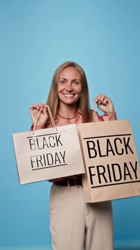 Portrait of happy Caucasian young adult woman holding Black Friday shopping bags and smiling at camera. Video suitable for seasonal retail sale promotions and shopping ads, vertical