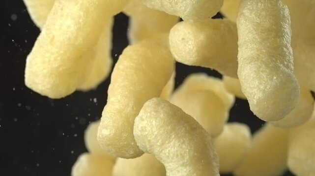 Corn sticks cheese puffs falling in super slow motion black background