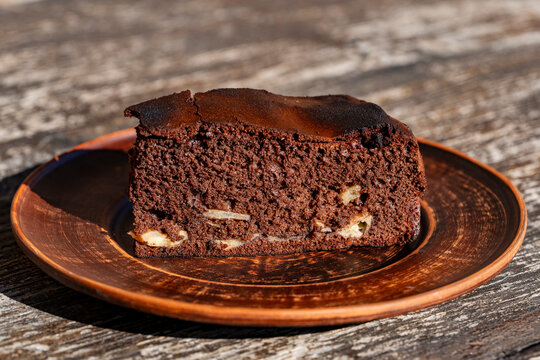 Slice homemade chocolate sponge cake on clay plate. Delicious piece dark chocolate brownie or biscuit cake with fruit filling served on rustic earthenware plate on table under bright sunlight