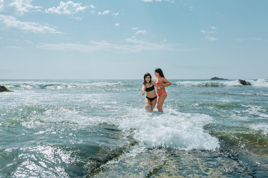 Two Girls Wading Into Ocean Waves, One Helping the Other