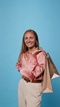 Portrait of smiling Caucasian young adult woman holding Black Friday shopping bags over shoulder. Clip suitable for retail promotions and seasonal discount sales advertising, vertical