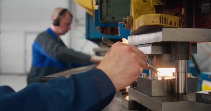 Hands of industrial worker positioning metal components for stamping. Close-up of factory workforce and technical skill