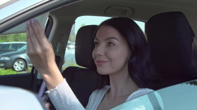 Young woman applying makeup with cosmetic soft makeup brush  in car using sun visor mirror. routine during a stop in a sunny parking area.