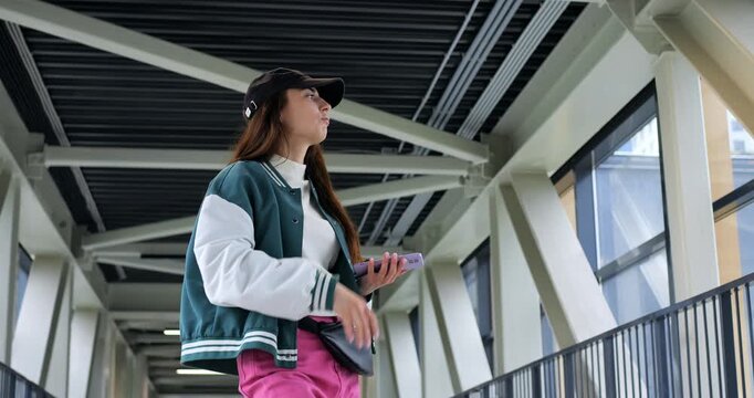 Teenage boy looks at skyline. Adolescent in jacket studies cityscape from covered walkway. Teenager wearing colorful clothing examines distant city skyline with curiosity from sheltered pathway