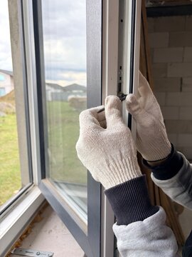 A worker adjusts the mechanism of a modern window frame. Manual window frame adjustment