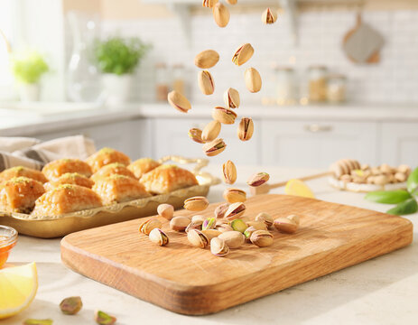 Healthy snacking and Mediterranean cuisine: pistachios falling onto a wooden board with baklava in a bright kitchen.