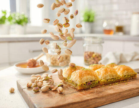 Healthy snacking and Mediterranean cuisine: pistachios falling onto a wooden board with baklava in a bright kitchen.