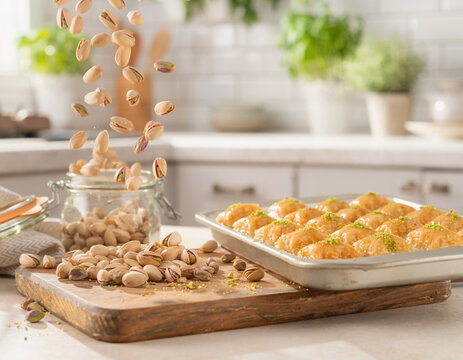Healthy snacking and Mediterranean cuisine: pistachios falling onto a wooden board with baklava in a bright kitchen.
