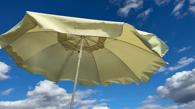 Yellow beach umbrella sways gently under blue sky with fluffy white clouds