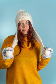 Woman wearing a warm hat and mittens against a blue background while smiling and posing
