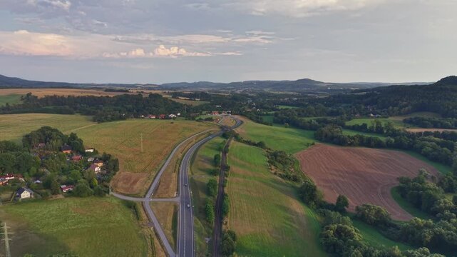 Elevated aerial perspective shows winding highway cutting across patchwork fields, passing rural homes and small village clusters, with aerial, drone, highway, road detail, showing interchange