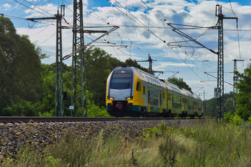 Modern yellow and green double-decker passenger train traveling on tracks in nature © Enrico Obergefäll